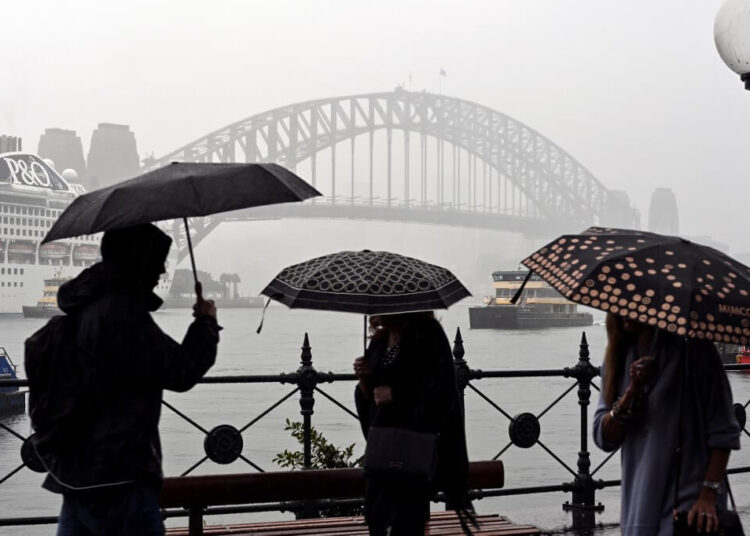 Pedestrians make their way in the rain along Sydney Harbour in Sydney on August 30, 2019. (Photo by Saeed KHAN / AFP)