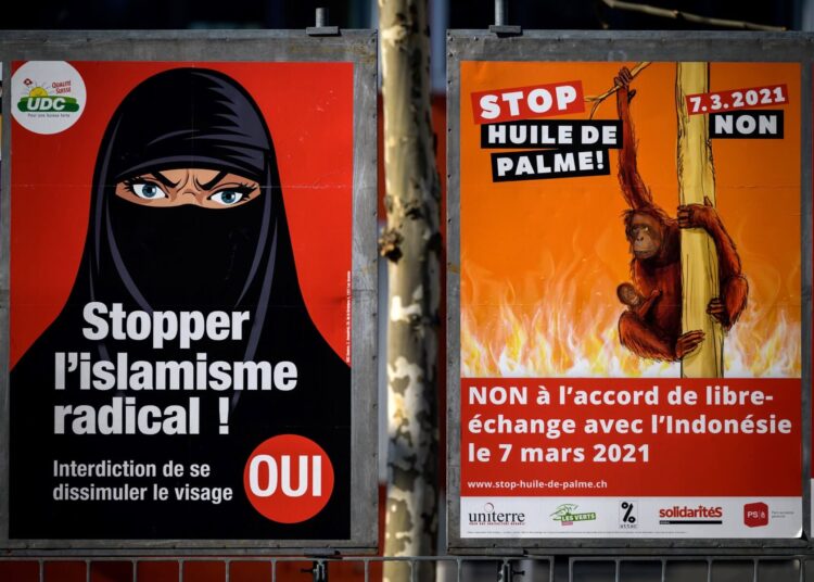 A photograph taken on March 1, 2021 in Geneva shows two campaign posters, one in favour of a "burqa ban" (L) initiative reading in French: "Stop Radical Islamism!" and the other (R) against a free trade agreement with Indonesia reading in French: "Stop palm oil! No to the free trade agreement with Indonesia on March 7, 2021" ahead of a nationwide vote by Swiss citizen. - Switzerland votes on March 7, 2021 on whether to ban full facial coverings in public places. The same day two other initiatives are being voted upon: a plan to introduce a federally-recognised electronic identity; and one concerning a trade agreement with Indonesia. (Photo by Fabrice COFFRINI / AFP)