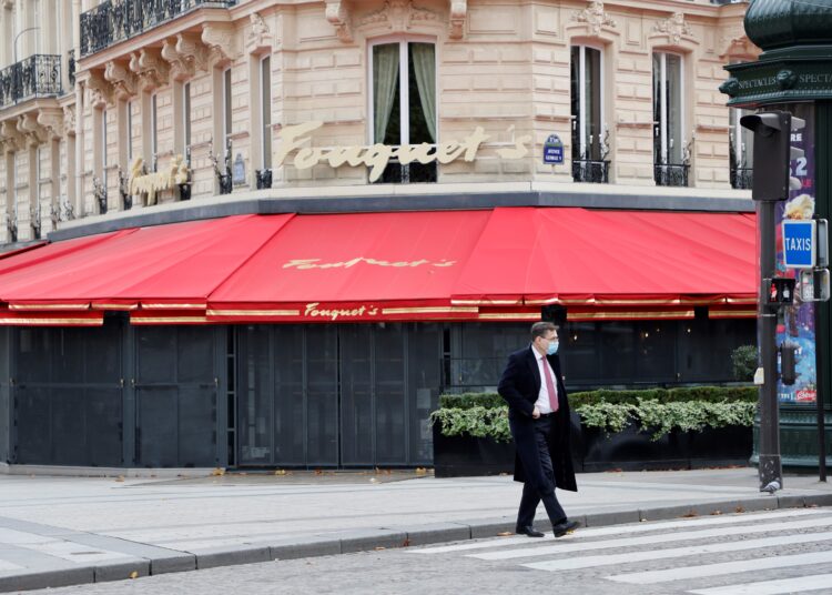 (FILES) In this file photo taken on November 2, 2020 a man, wearing a protective mask, walks past the closed terrace of the Fouquet's restaurant on the Champs-Elysee avenue on the fourth day of a lockdown aimed at containing the spread of the novel coronavirus (Covid-19) in Paris. - The restaurateurs are in the starting blocks to once again welcome customers wishing to invest their terraces after six months of closure. The year 2020 has been a nightmare and the reopening of restaurants remains without a scheduled date, but President Emmanuel Macron told mayors on April 15, 2021 evening that he still intended to reopen terraces, with museums, from mid-May. (Photo by Ludovic MARIN / AFP)