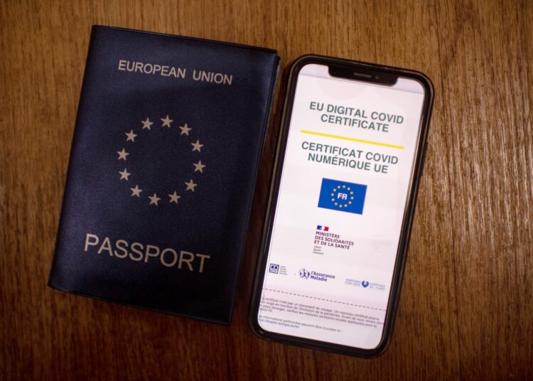 A picture taken on June 29, 2021 in Paris shows a passeport next to a mobile phone whose screen bears a EU Digital Covid certificate. - The European health certificate, which Belgium began using on June 16, 2021, will become operational across the EU on July 1, 2021. (Photo by Olivier MORIN / AFP)