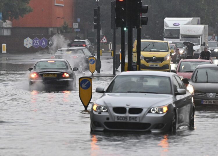 A car (L) overheats on a flooded road in The Nine Elms district of London on July 25, 2021 during heavy rain. - Buses and cars were left stranded when roads across London flooded on Sunday, as repeated thunderstorms battered the British capital. (Photo by JUSTIN TALLIS / AFP)