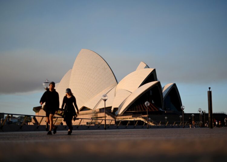 People walk near the Opera House in Sydney on August 14, 2021, as Australia's biggest city announced tighter Covid restrictions including heavier fines and tighter policing to contain a Delta outbreak. (Photo by Saeed KHAN / AFP)