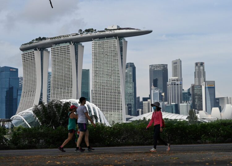 People walk along Marina Bay East Park near the financial business district in Singapore on October 20, 2021. (Photo by Roslan RAHMAN / AFP)