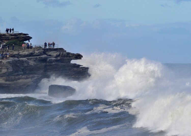 Residents watch big waves crashing into rocks at Bondi Beach in Sydney on April 2, 2022, amid danger warnings issued for most of the coast in New South Wales as strong winds whipped up damaging waves. (Photo by Muhammad FAROOQ / AFP)