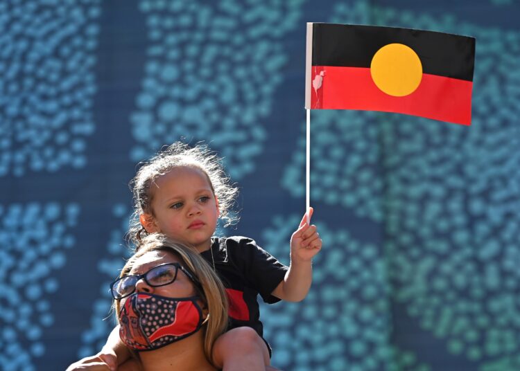 A young girl holds up an Australian Aboriginal flag during an "Invasion Day" demonstration on Australia Day in Sydney on January 26, 2022. (Photo by Steven Saphore / AFP)