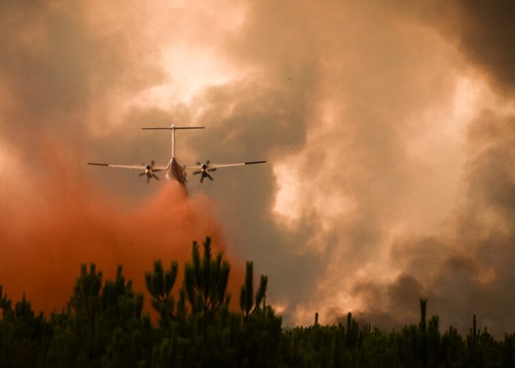A Dash 8 firefighting aircraft sprays fire retardant over trees during a wildfire near Belin-Beliet in Gironde, southwestern France, on August 10, 2022. (Photo by Philippe LOPEZ / AFP)