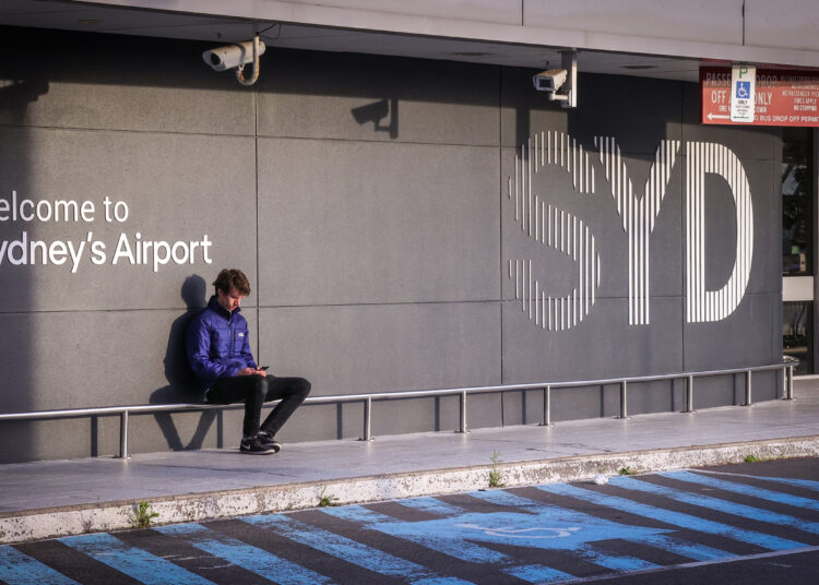 This picture taken on September 29, 2020 shows a man sitting outside the departures area of the Sydney International Airport as he waits to check in for a flight in Sydney. (Photo by David GRAY / AFP)