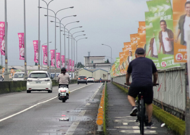 This picture taken on November 22, 2022 shows commuters riding past election campaign flags on a bridge in Yilan county. (Photo by Sam YEH / AFP)