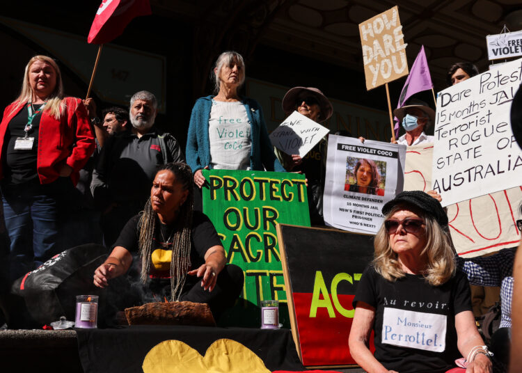 Protesters hold placards during a rally in support of climate activist Deanna "Violet" Coco, who helped block the Sydney Harbour Bridge last April and was sentenced to jail, outside the Downing Centre Local and District Court building in Sydney, December 13, 2022. (Photo by DAVID GRAY / AFP)